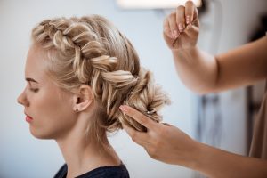 Female hairdresser making hairstyle to beautiful blonde girl in beauty salon. Copy space.